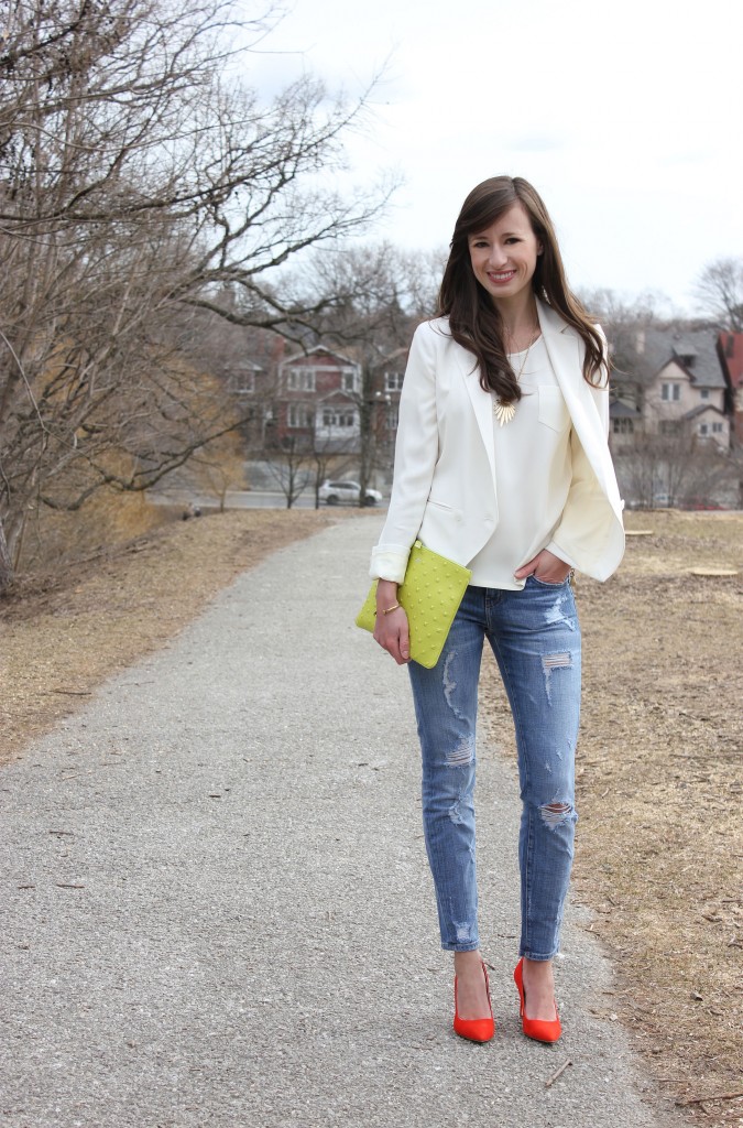 Girl in white blazer, jeans and red heels with a green bag.